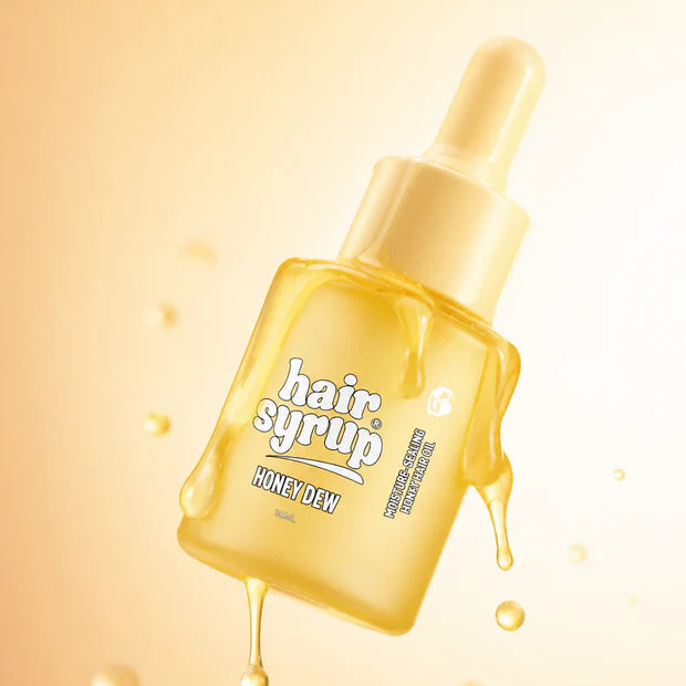 A bottle of honey syrup hair oil with a dropper cap, floating diagonally against a warm golden-yellow background with stylized honey droplets dripping from the bottle.